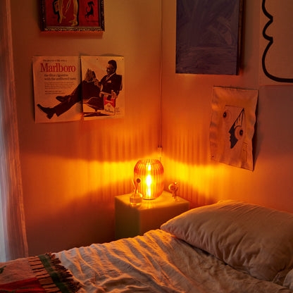 Allium Lamp by Wooj Design featuring a warm amber glass shade, styled on a wooden surface with decorative books and plants.