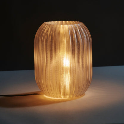 Wooj Design Allium Lamp with clear glass shade and floral-inspired design, displayed on a wooden surface in a modern interior setting.