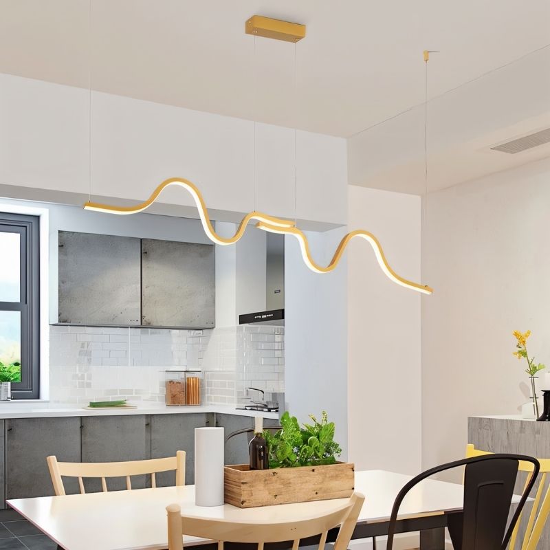 Lissar gold wave pendant light by Residence Supply hanging over a dining table, modern gold fixture with a flowing wave design