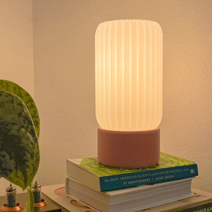 Terra Labs Milk Shade Barrel Table Lamp with white ceramic base and cylindrical milk-colored fabric shade on a wooden table.