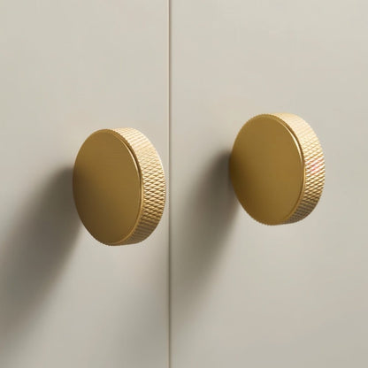 Cylindrical knurled Noah cabinet knob in matte black, made of metal, mounted on a wooden cabinet for modern kitchen decor.