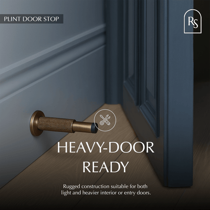 Residence Supply Plint Door Stop shown in black with a simple design, placed on a wooden floor to prevent door movement.