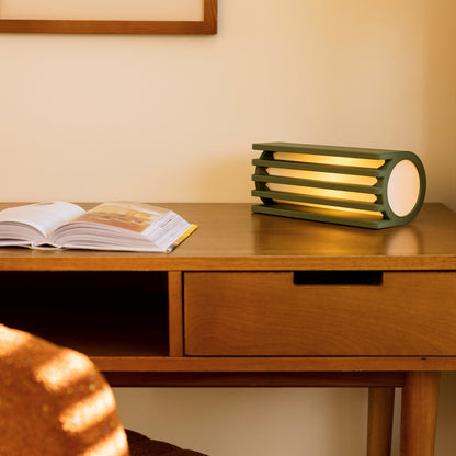 Terra Labs radiator-shaped olive green table lamp with a sleek, modern design on a wooden surface.
